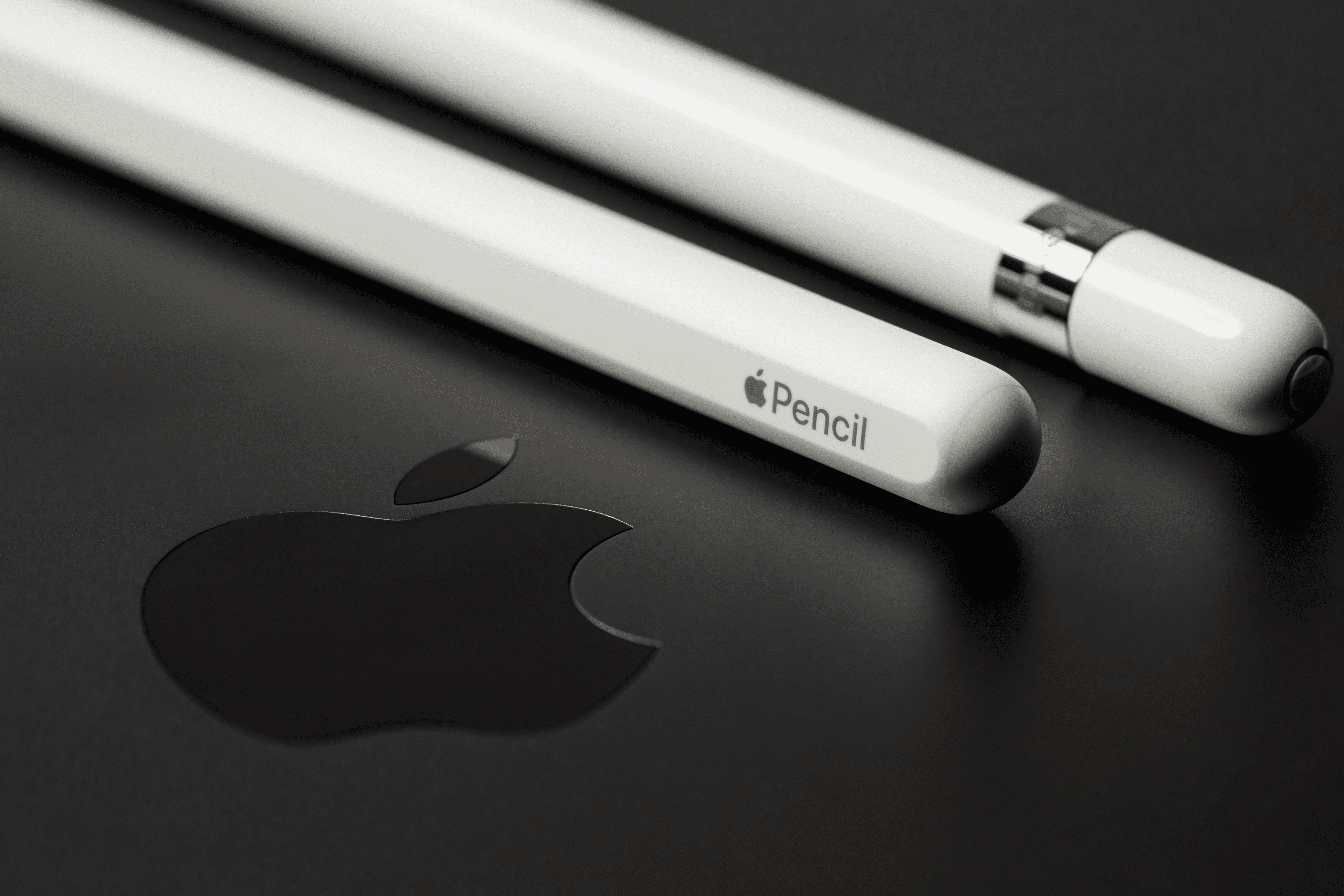 Comparación del Apple Pencil de primera y segunda generación en primer plano con fondo negro y el logotipo de Apple.